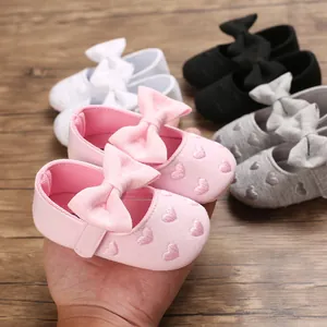Dettaglio di scarpine da principessa per neonata con ricamo a cuore e un grande fiocco