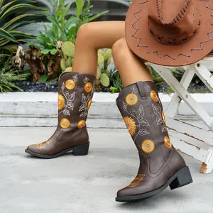 Vista detallada de botas de vaquero marrones con bordado de girasol en un jardín