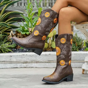 Botas altas bordadas en marrón con motivos de girasol y tacón grueso usadas al aire libre.