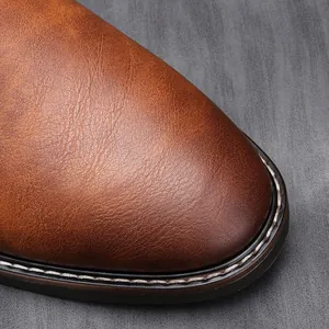Gros plan sur l'embout en cuir marron patiné des bottines Chelsea rétro avec coutures blanches.