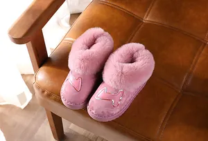 Rosa Kinder-Schneestiefel mit dickem Kunstfellfutter auf braunem Lederstuhl Detailansicht.