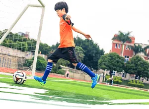 Action shot showing the vibrant blue children's soccer shoes on an artificial turf