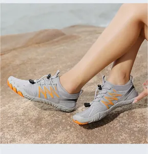 Zapatos de agua grises y naranjas usados por un modelo en una playa rocosa soleada.