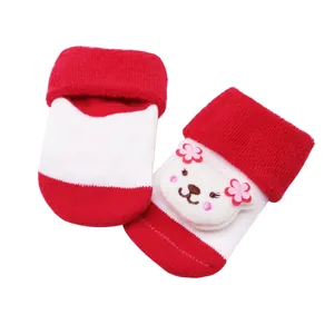 Gros plan d'une poupée ours mignonne sur des chaussettes de bébé épaisses rouges et blanches.