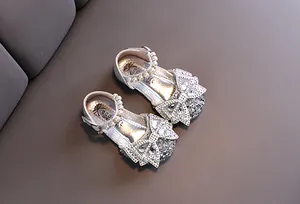 Detalle de zapatos de princesa plateados con purpurina para niña con lazo y perlas.