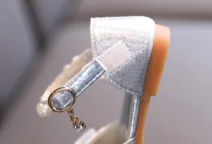 Detalle macro de zapato plateado con purpurina para niña con correa de perlas y colgante