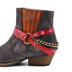 Gros plan de bottines en daim avec des lanières à fleurs rouges et chaîne dorée