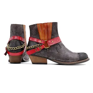 Vue détaillée de bottines cowboy en cuir dépoli avec sangle rouge et détails de chaînes.