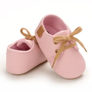 Detailed close-up view of pink soft-soled baby walking shoes featuring brown laces
