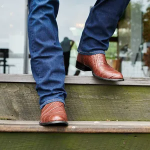 Vue détaillée de bottes de cowboy western marron à motif crocodile sur des marches en bois