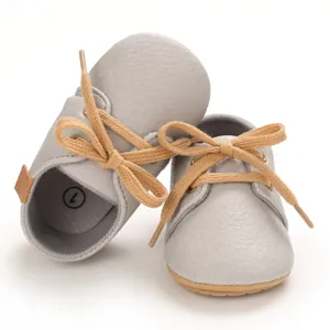 Detailed view of grey pebbled leather infant walker shoes featuring camel laces and soft soles.
