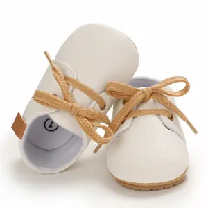 Close-up of white soft-soled baby walking shoes with tan laces for infants aged 0-1.