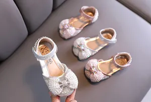 Detalle de lazos de perlas y pedrería en zapatos de princesa para niña en varios colores.
