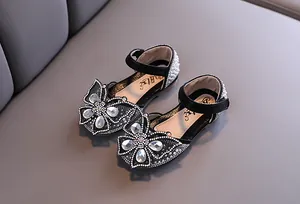 Détail de chaussures de princesse noires pour filles avec un nœud papillon en strass et perles.