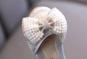 Detalle de un lazo brillante adornado con perlas y pedrería en un zapato de princesa.