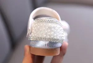 Primer plano detallado de diamantes de imitación y perlas en un zapato de baile plateado para niña