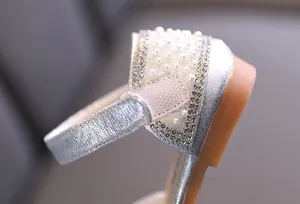 Primer plano de los exquisitos detalles de diamantes y perlas en zapatos de niña plateados