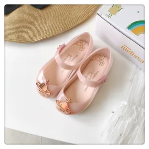Primer plano de sandalias de gelatina rosa con un emblema metálico de Saturno en oro rosa.