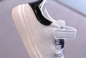 Dettaglio di sneakers in pelle bianca per bambini con tallone in vernice nera e velcro