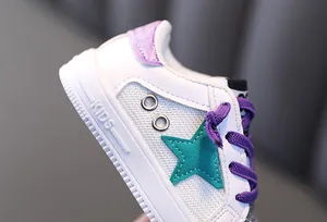 Close-up detail of kids white sneaker with mesh panels and green star patch