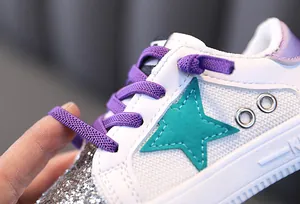 Detail of white children's sneaker featuring purple laces and a teal star patch