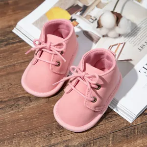 Close-up view of adorable pink lace-up baby boots on a magazine and rustic wooden surface