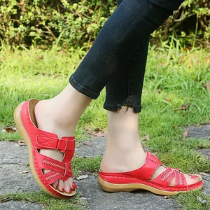 Close-up view of stylish red wedge sandals with cutout design worn on a grassy path