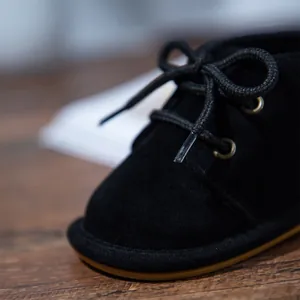 Detailed macro view of black suede baby walking shoe showing laces and gum sole texture