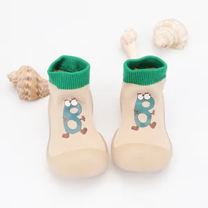 Detailed view of beige baby sock shoes with green ribbing and cute cartoon character