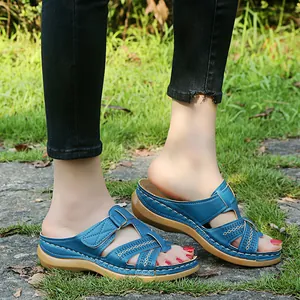 Detail view of blue wedge sandals with hollow-out cross straps and thick sole worn on grass