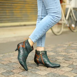 Gros plan de bottines rétro vert métallisé avec talons aiguilles sur des pavés rustiques.