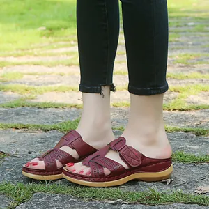 Close-up of burgundy wedge sandals with cross strap and hollow design on stone path