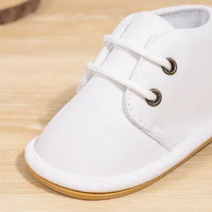 Macro detail view of white lace-up infant baby shoes featuring non-slip rubber soles