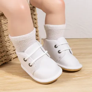 Close-up of white lace-up baby walking shoes with rubber soles on a mannequin foot.