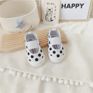 Vista detallada de zapatos de lona para niños pequeños con lunares negros sobre tabla decorativa.