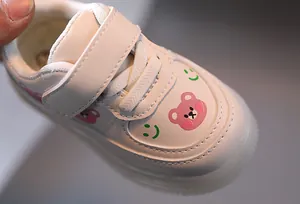 Detailed macro shot of white toddler light-up sneaker with pink bear and smiley pattern