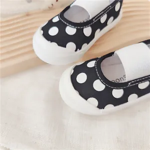 Primer plano de zapatos de lona para bebés con lunares blancos y negros y cinta elástica