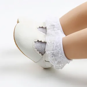 Close-up of white baby girl princess shoes with delicate lace socks and soft rubber sole.