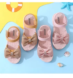 Detail view of girls' summer sandals with sparkling rhinestone bows on soft pink and beige soles.