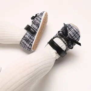 Makroaufnahme von blau-karierten Babyschuhen mit schwarzen Schleifen und Rippsocken.