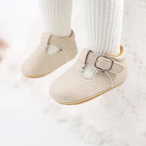 Close-up of beige baby girl Mary Jane shoes with scalloped edges and a metal buckle.