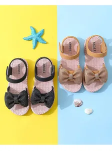 Detailed view of girls' beach sandals with sparkling bow ties in black and gold