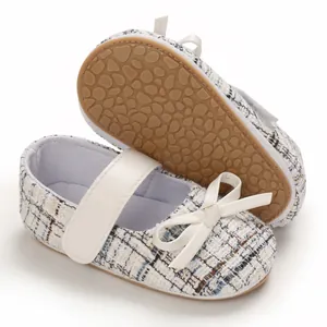 Nahaufnahme von Baby-Lauflernschuhen aus Tweed mit weißer Schleife und rutschfester Sohle.