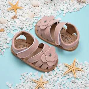 Vue de dessus de sandales roses pour bébé avec fleurs sur un décor de plage bleu.