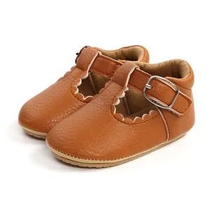 Close-up detail of brown leather baby girl shoes with scalloped edges and buckle strap