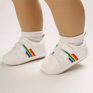 Détail de chaussures de marche blanches pour bébé avec rayures arc-en-ciel et velcro