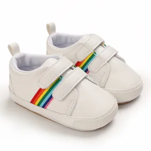 Gros plan de chaussures de marche blanches pour bébé avec rayures arc-en-ciel et semelle souple