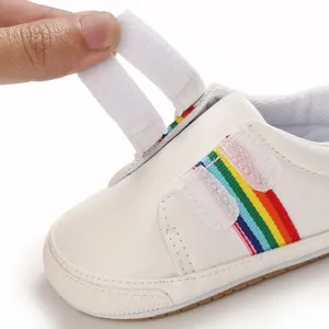 Détail de chaussure de marche pour bébé blanche avec rayures arc-en-ciel et scratch