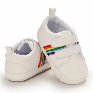 Gros plan de chaussures de marche bébé blanches avec rayures arc-en-ciel et semelle souple.