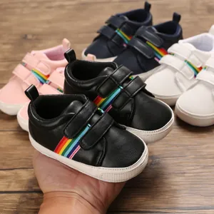 Gros plan de chaussures de marche pour bébé noires avec rayures arc-en-ciel et semelles
